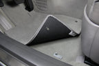 Car interior with a gray floor mat and a speaker grille.