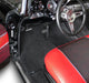 Close-up of a classic car's interior with red seats and black floor mat.