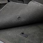 Close-up of a textured car mat with a button on a gray carpeted floor.
