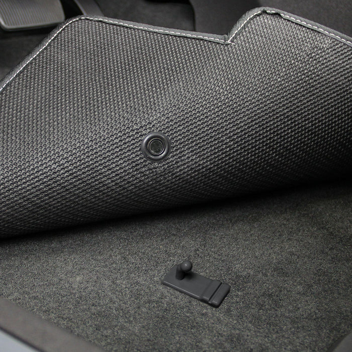 Close-up of a textured car mat with a button on a gray carpeted floor.