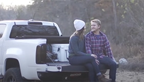 A couple sitting on a tailgate with the tonneau opened