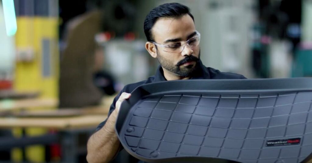 Man holds and inspects one of his clean, heavy-duty, custom all-weather mat from his truck